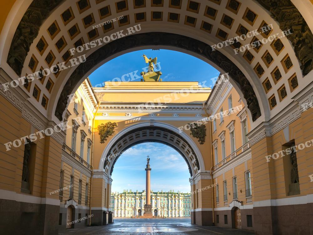На фотографии изображена арка Главного штаба и Александровская колонна на Дворцовой площади в Санкт-Петербурге. Вид через арку открывает величественное здание Зимнего дворца и центральную часть площади. Утреннее солнце подчеркивает архитектурные детали и создает атмосферу величия и истории. Дворцовая площадь является важной исторической и культурной точкой города.